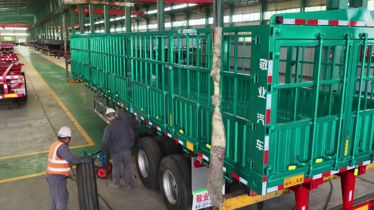 Workers fitting a wheel to a fence semi trailer on the assembly floor